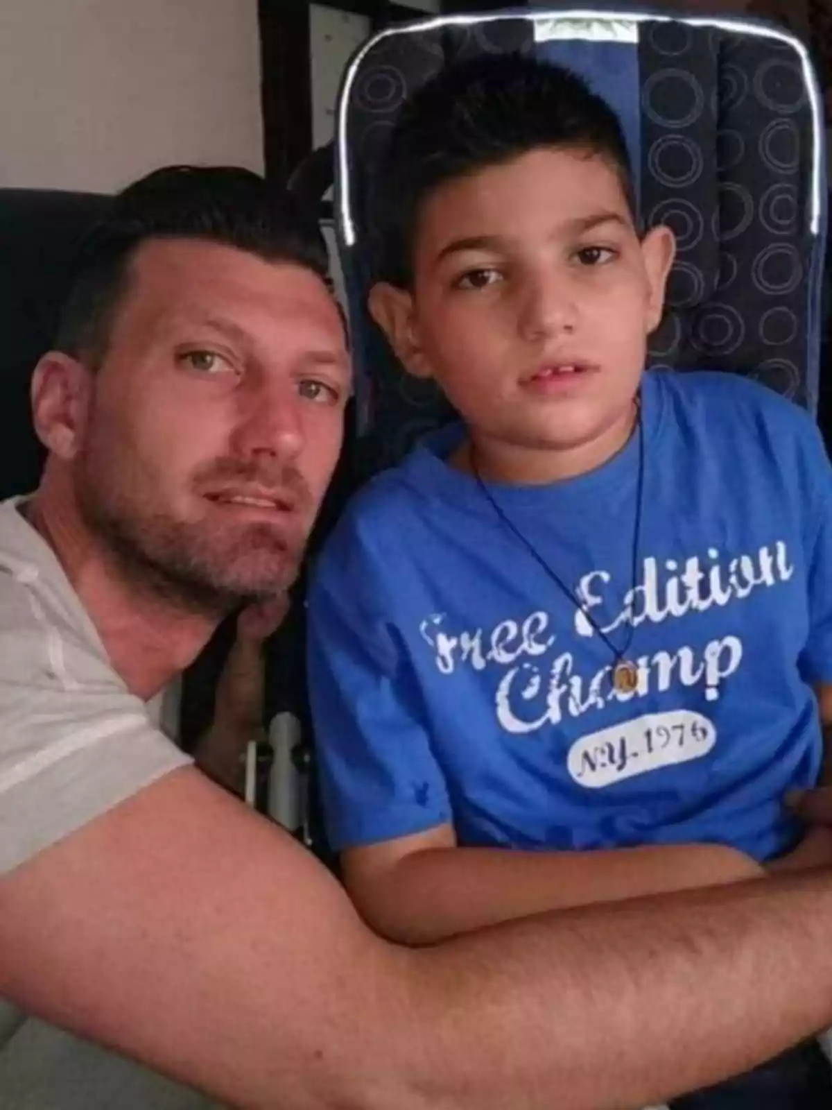 Un hombre y un niño posan juntos para una foto, el niño lleva una camiseta azul con la inscripción 