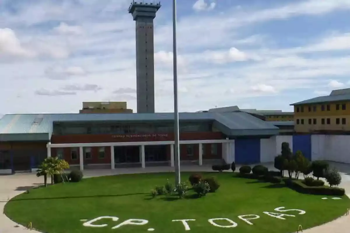 Imagen de la entrada principal del Centro Penitenciario de Topas, con una torre de vigilancia prominente y un jardín bien cuidado en el frente.