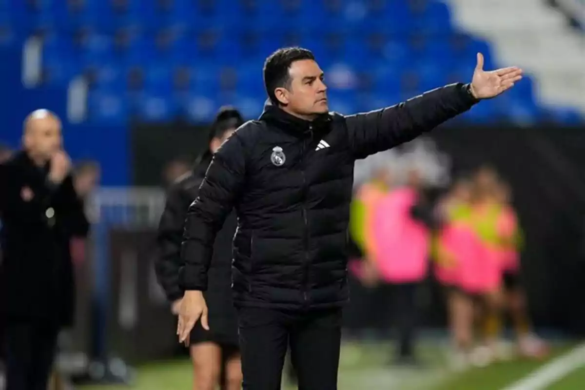 Un entrenador de fútbol con chaqueta negra gesticula en el campo durante un partido. Un entrenador de fútbol con chaqueta negra gesticula en el campo durante un partido.
