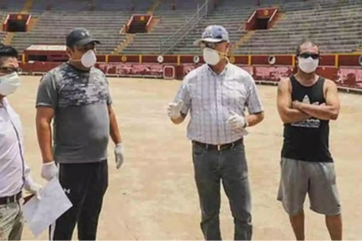 Un grupo de personas con mascarillas y guantes se encuentra en una plaza de toros, aparentemente discutiendo o planificando algo. Un grupo de personas con mascarillas y guantes se encuentra en una plaza de toros, aparentemente discutiendo o planificando algo.