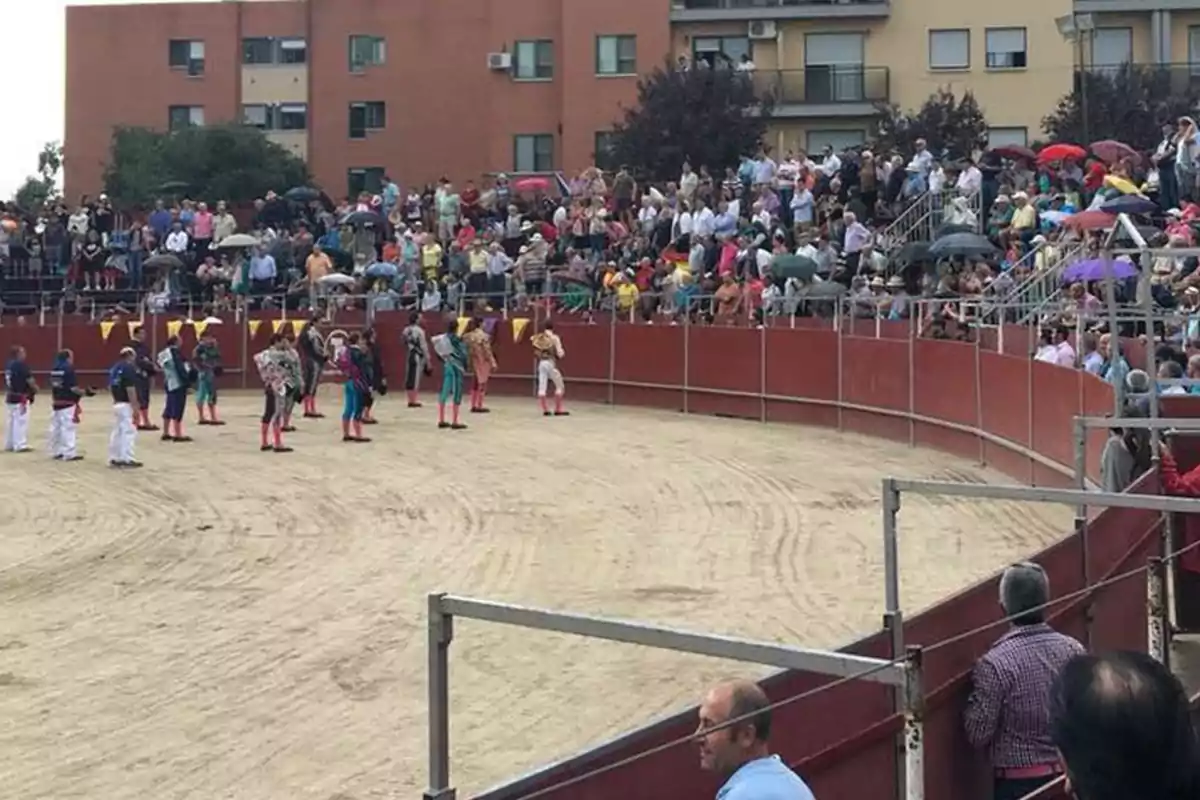 Una multitud de personas observa un evento en una plaza de toros, donde varios participantes vestidos con trajes coloridos están en el centro de la arena.