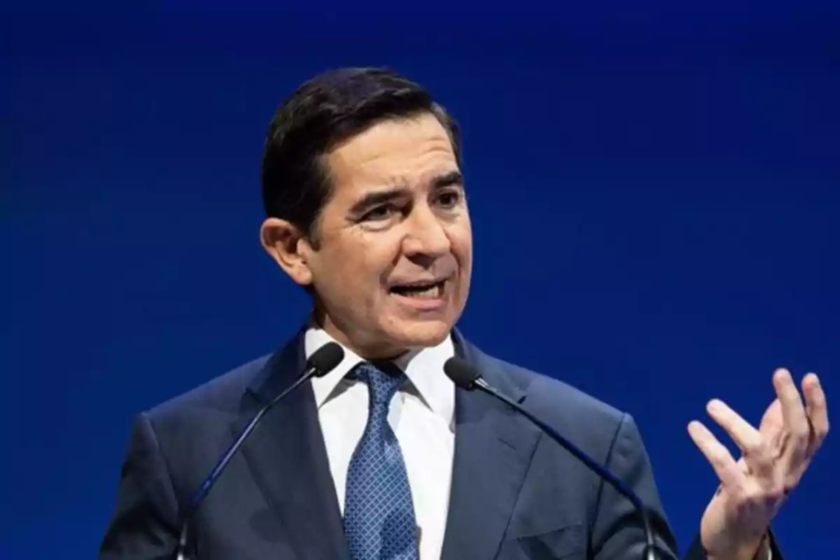 Un hombre en traje hablando en un escenario con fondo azul. Un hombre en traje hablando en un escenario con fondo azul.