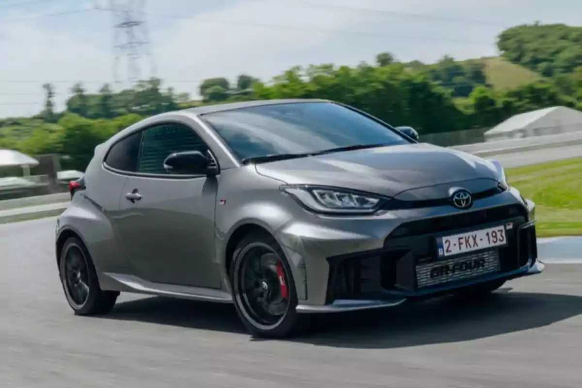 Un auto deportivo gris en una pista de carreras rodeada de vegetación. Un auto deportivo gris en una pista de carreras rodeada de vegetación.