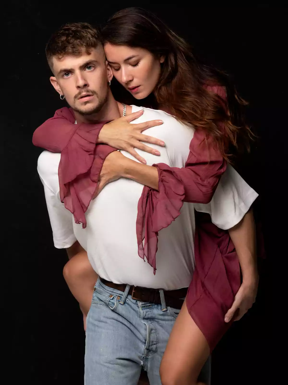 Una mujer con los ojos cerrados abraza a un hombre desde atrás, mientras él mira al frente con una expresión seria.