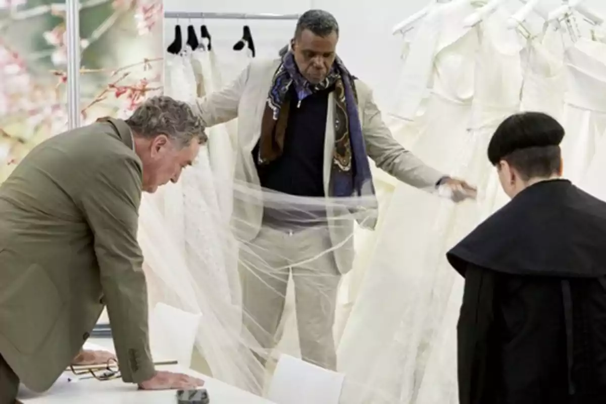 Tres personas observan y manipulan vestidos de novia en una tienda de ropa.