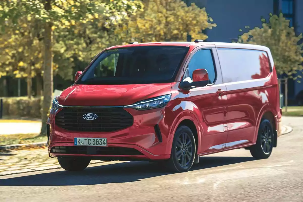 Una furgoneta FORD TRANSIT CUSTOM roja circulando por una carretera rodeada de árboles.