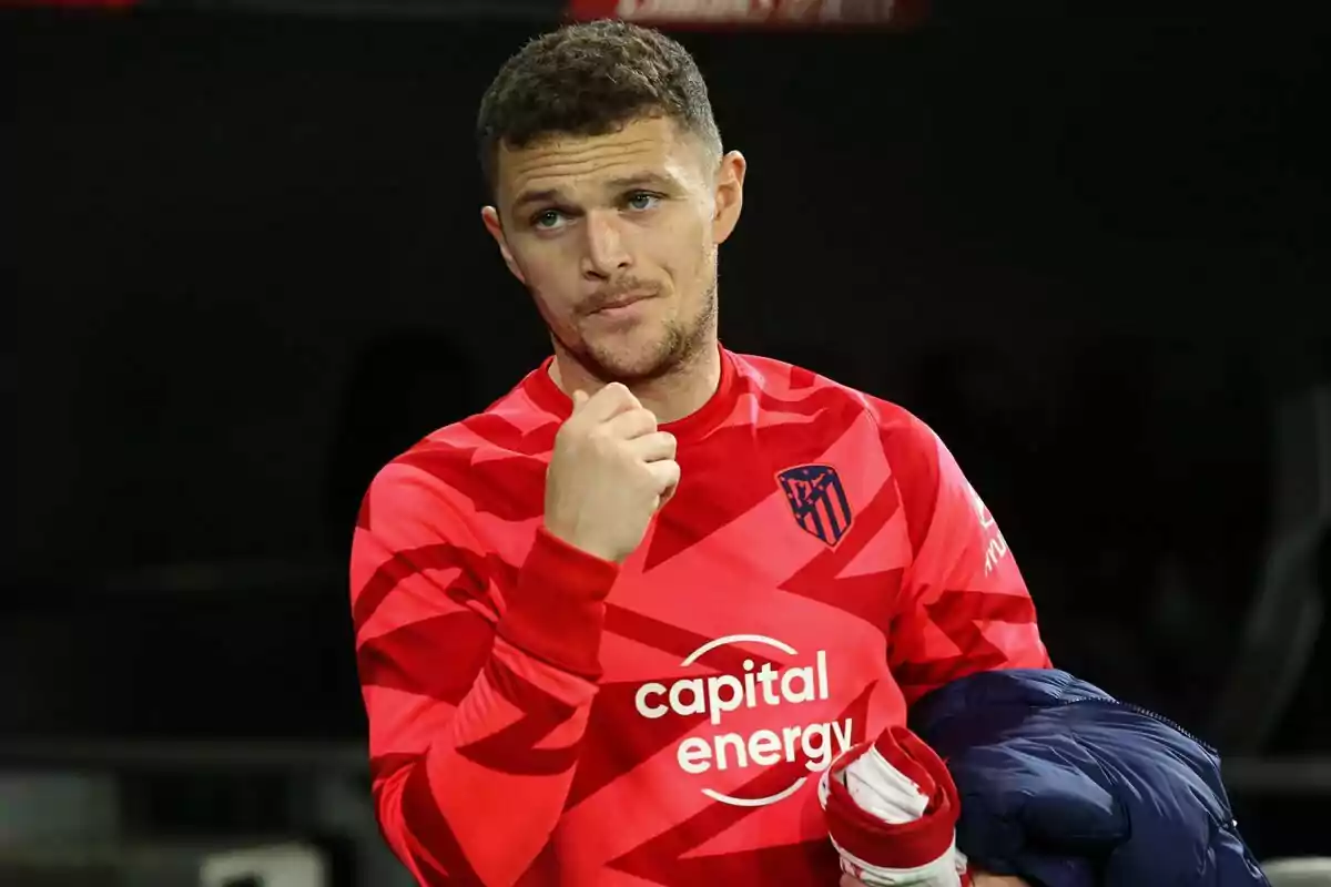 Un jugador de fútbol con uniforme rojo del Atlético de Madrid sostiene una chaqueta azul. Un jugador de fútbol con uniforme rojo del Atlético de Madrid sostiene una chaqueta azul.