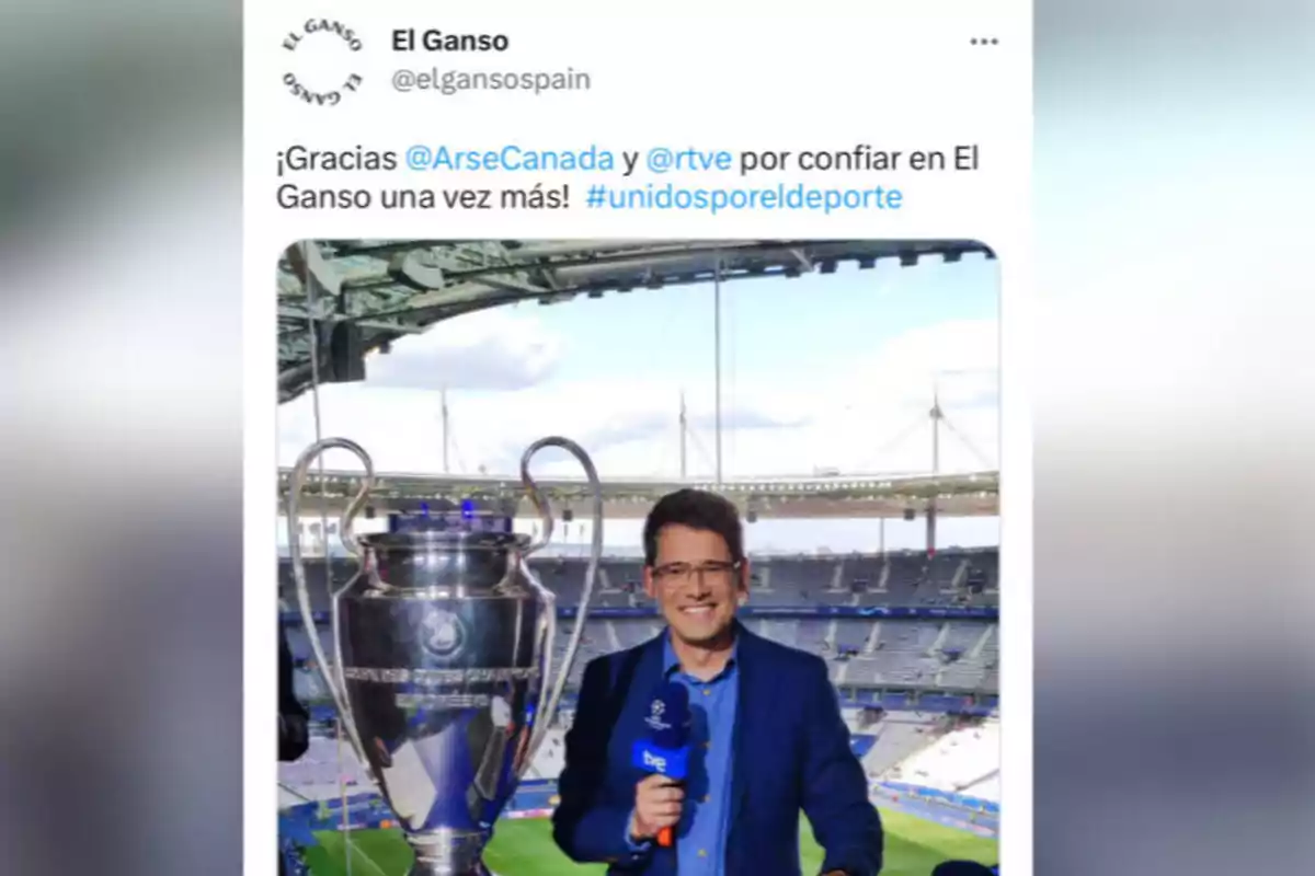 Un hombre con gafas y un micrófono de rtve está de pie junto a un gran trofeo en un estadio de fútbol vacío, con un mensaje de agradecimiento de El Ganso a ArseCanada y rtve en la parte superior. Un hombre con gafas y un micrófono de rtve está de pie junto a un gran trofeo en un estadio de fútbol vacío, con un mensaje de agradecimiento de El Ganso a ArseCanada y rtve en la parte superior.