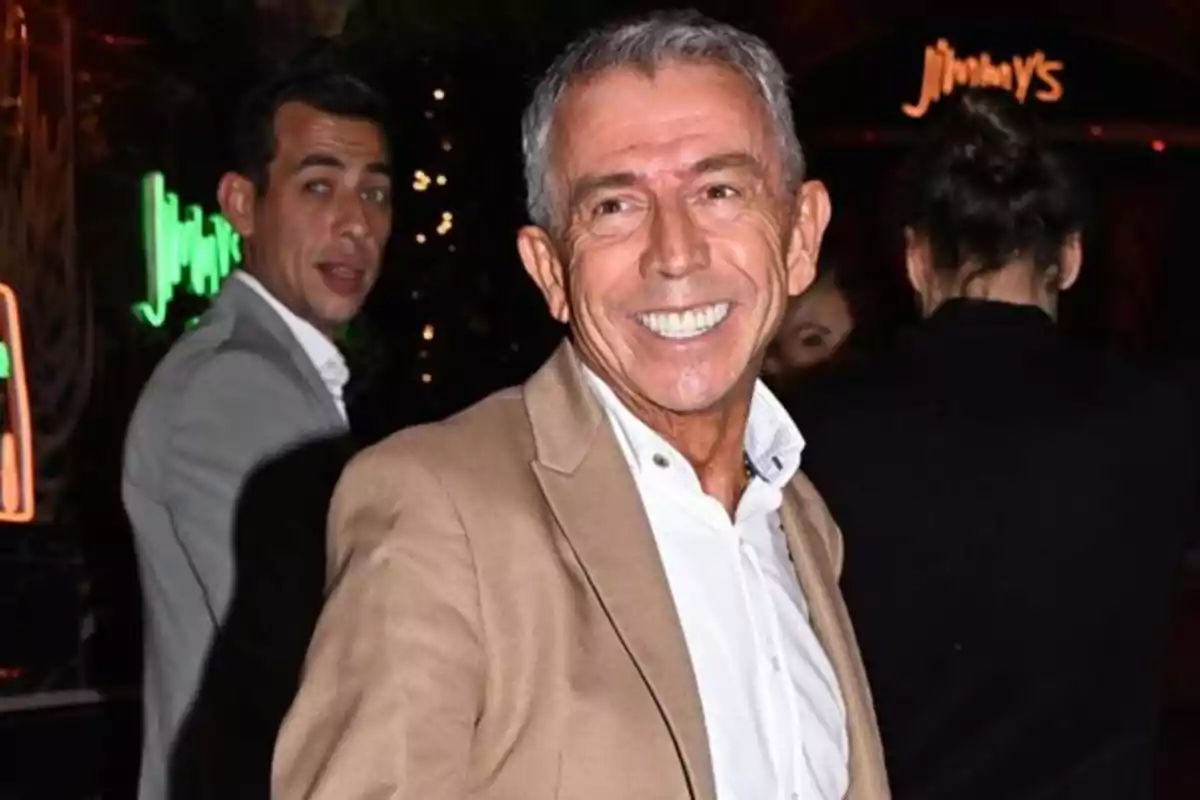 Un hombre sonriente con chaqueta beige y camisa blanca en un evento nocturno.