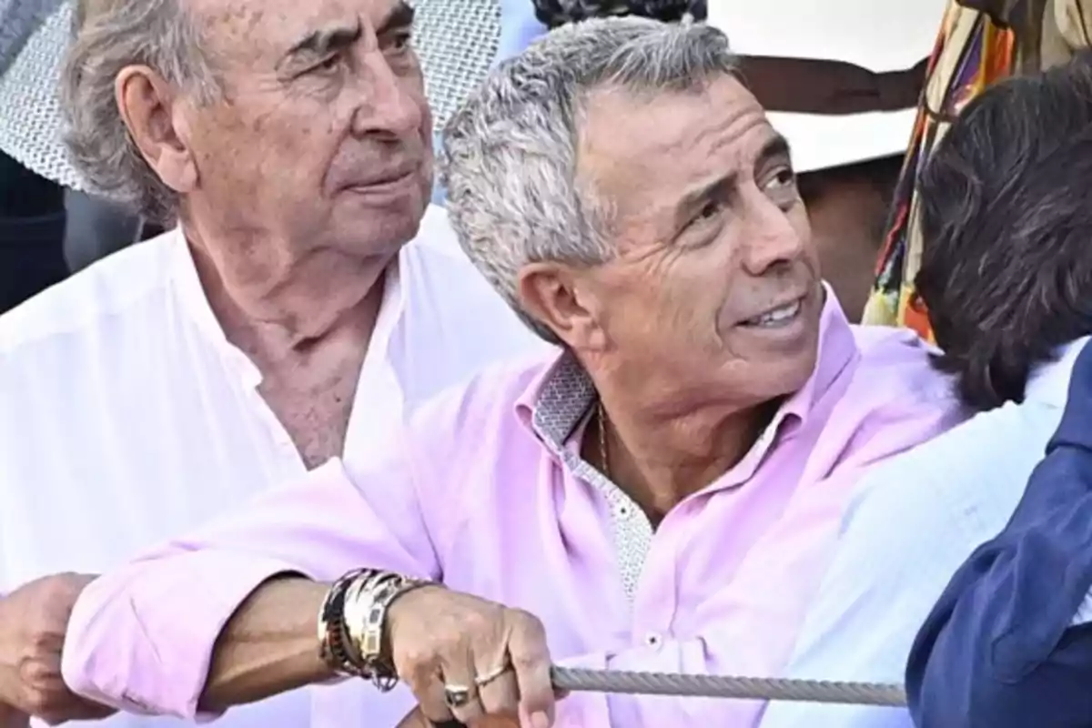 Dos hombres mayores participando en un juego de tirar de la cuerda, uno de ellos lleva una camisa rosa y varias pulseras.