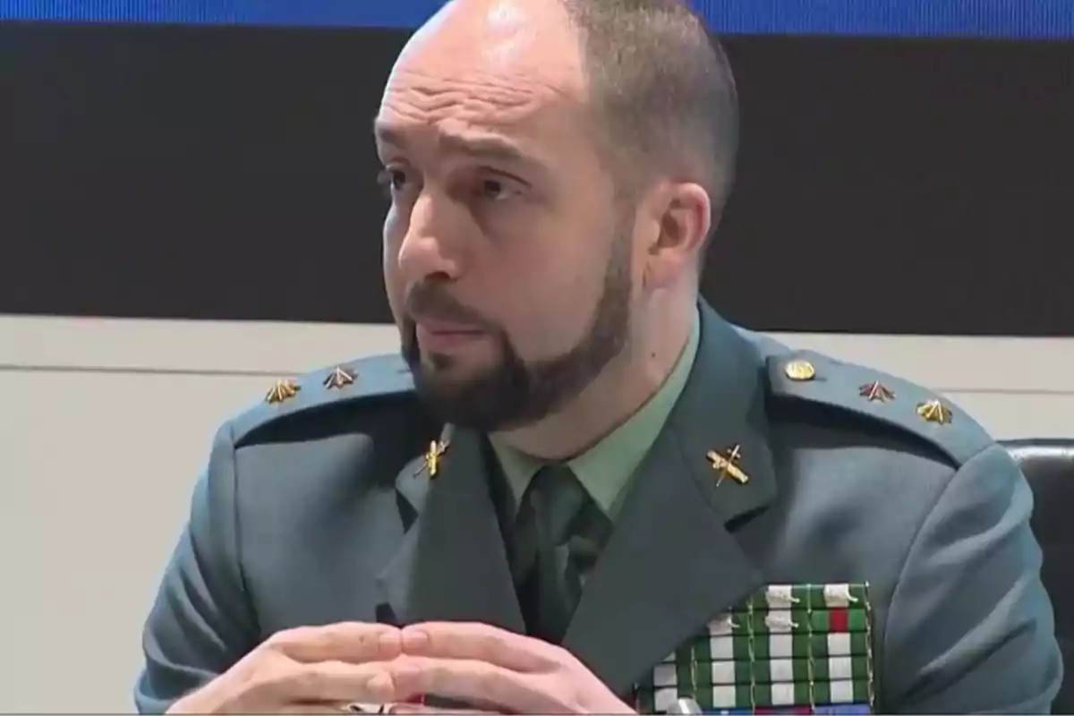 Hombre con uniforme militar verde sentado y hablando en una conferencia Hombre con uniforme militar verde sentado y hablando en una conferencia