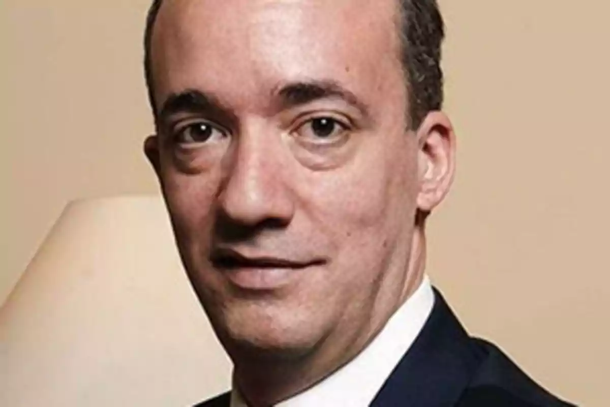 Hombre de traje oscuro mirando a la cámara con expresión seria y fondo beige Hombre de traje oscuro mirando a la cámara con expresión seria y fondo beige