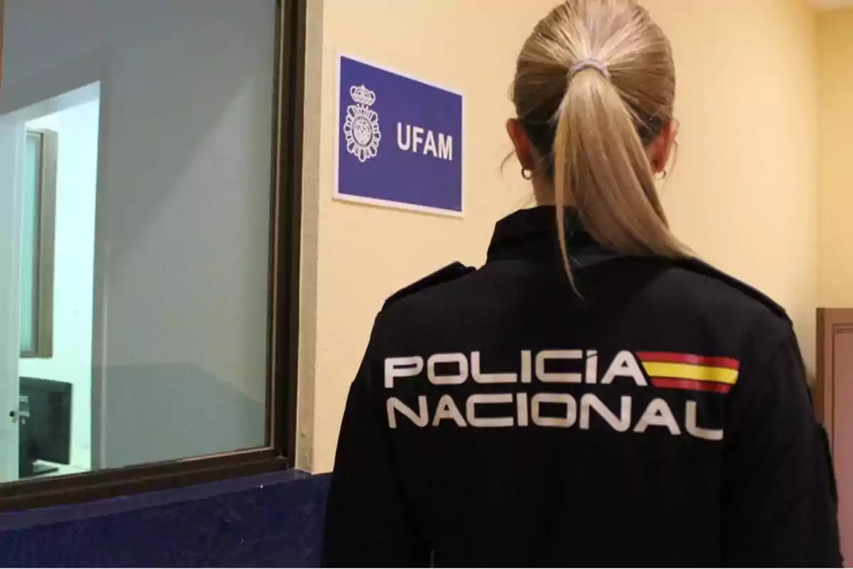 Una agente de la Policía Nacional de espaldas frente a una puerta con un cartel que dice 