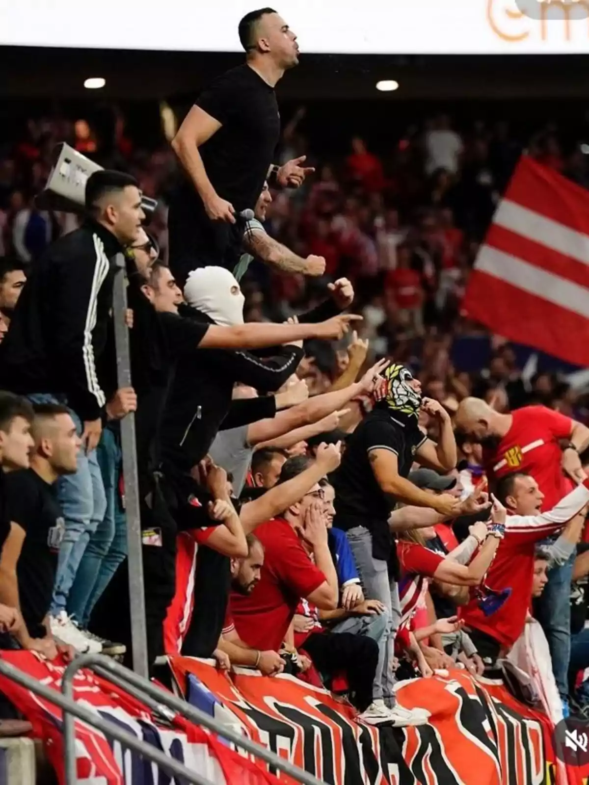 Aficionados de un equipo de fútbol animando apasionadamente desde las gradas, algunos de ellos con gestos y expresiones de entusiasmo.