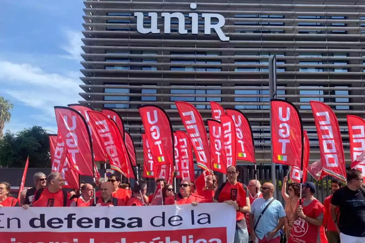 Manifestación de personas con banderas rojas de UGT frente a un edificio con el letrero "unir".