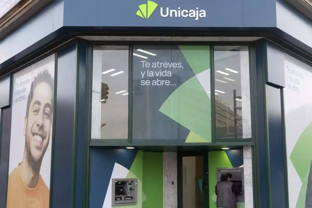 Fachada de una sucursal de Unicaja con un cajero automático y un cartel publicitario que dice 