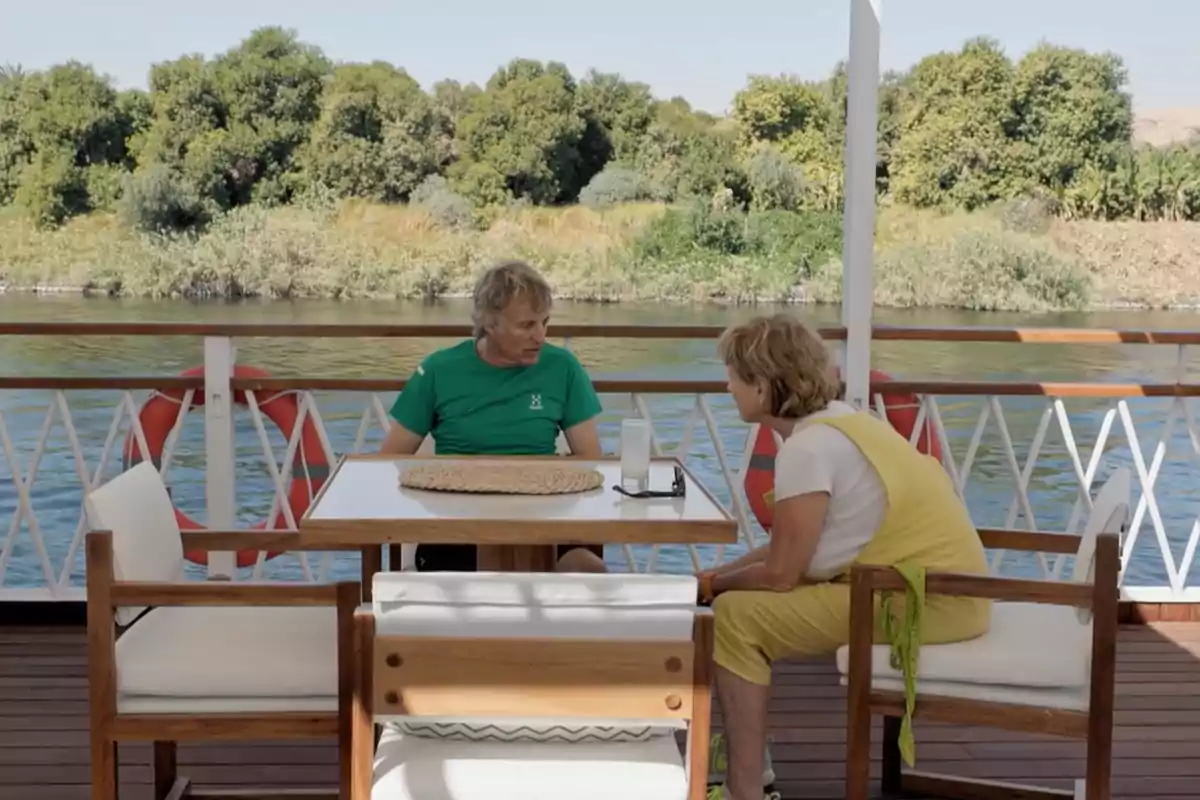 Jesús Calleja y Mercedes Milá conversan en una mesa al aire libre en un barco con un paisaje de árboles y agua de fondo. Captura de 'Universo Calleja' Jesús Calleja y Mercedes Milá conversan en una mesa al aire libre en un barco con un paisaje de árboles y agua de fondo. Captura de 'Universo Calleja'
