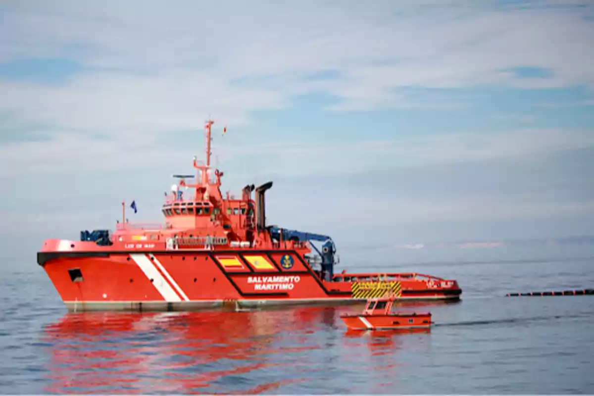 Un barco de Salvamento Marítimo de color rojo en el mar con una pequeña embarcación a su lado.