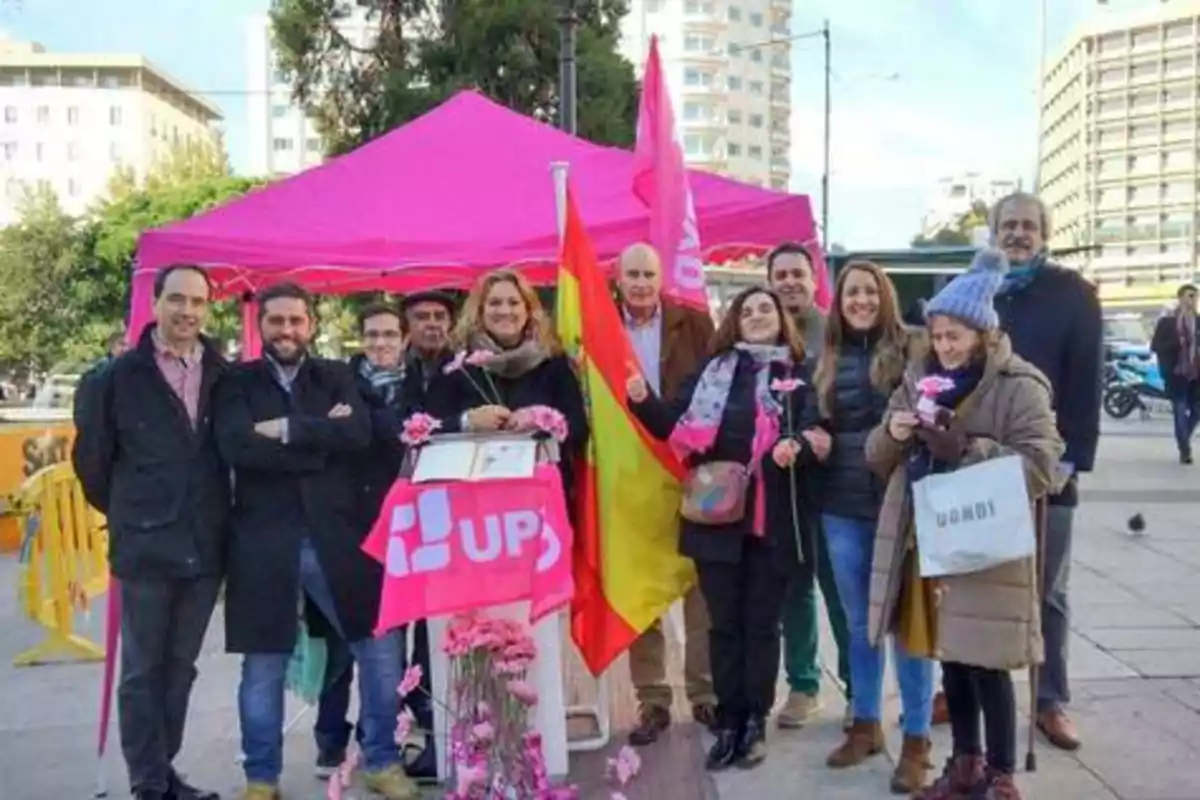 Un grupo de personas posando frente a una carpa rosa con banderas y flores.