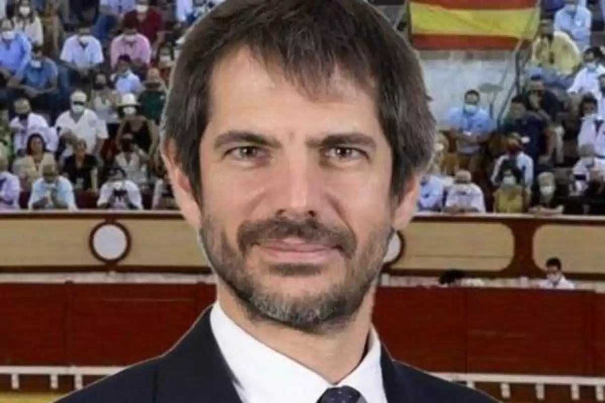 Un hombre con barba y cabello oscuro, vestido con traje y corbata, está frente a una multitud en lo que parece ser una plaza de toros.