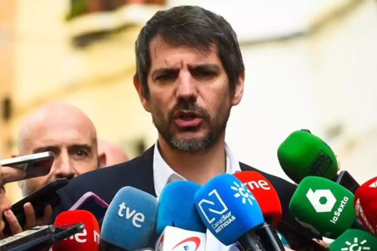 Un hombre hablando frente a varios micrófonos de diferentes medios de comunicación. Un hombre hablando frente a varios micrófonos de diferentes medios de comunicación.