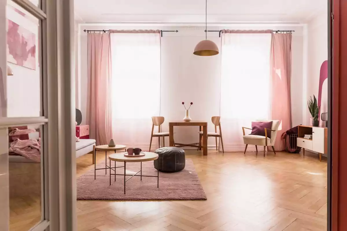 Una sala de estar luminosa con cortinas rosadas, muebles de madera clara, una alfombra rosa, y una decoración minimalista.
