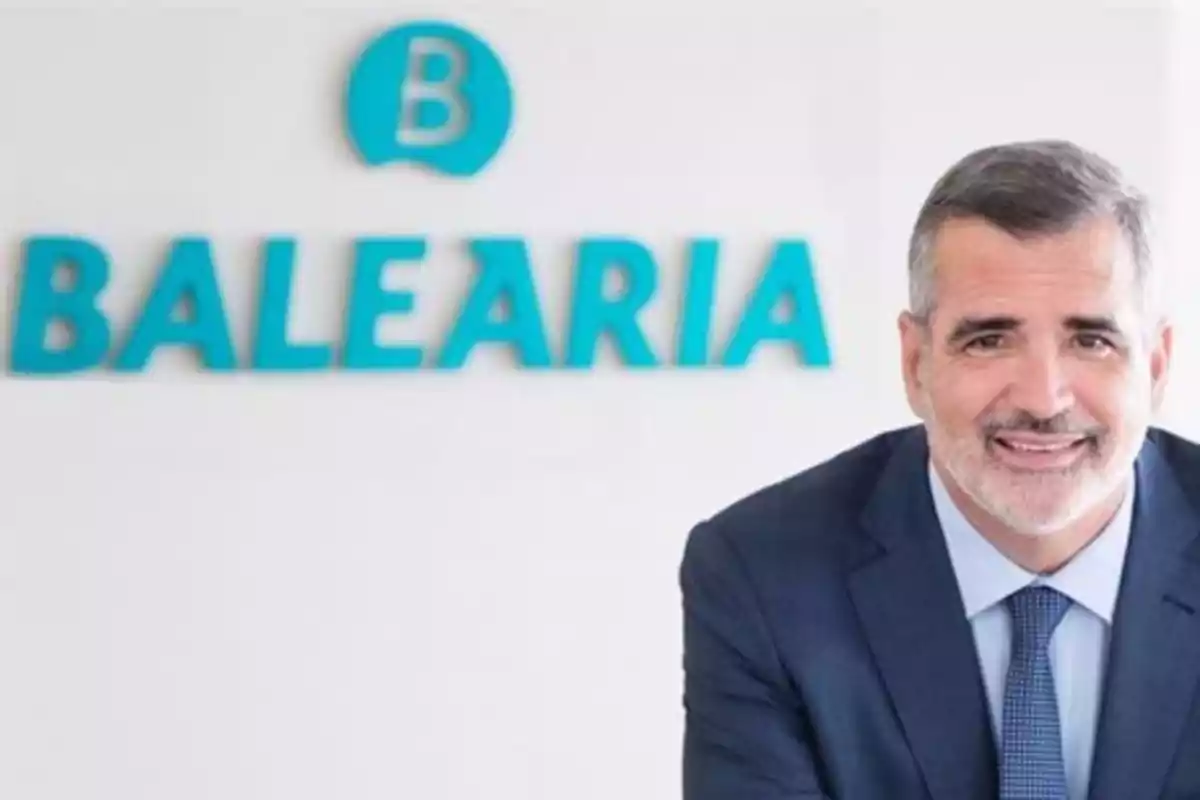 Un hombre con traje sonríe frente a un logotipo de Balearia en una pared blanca.