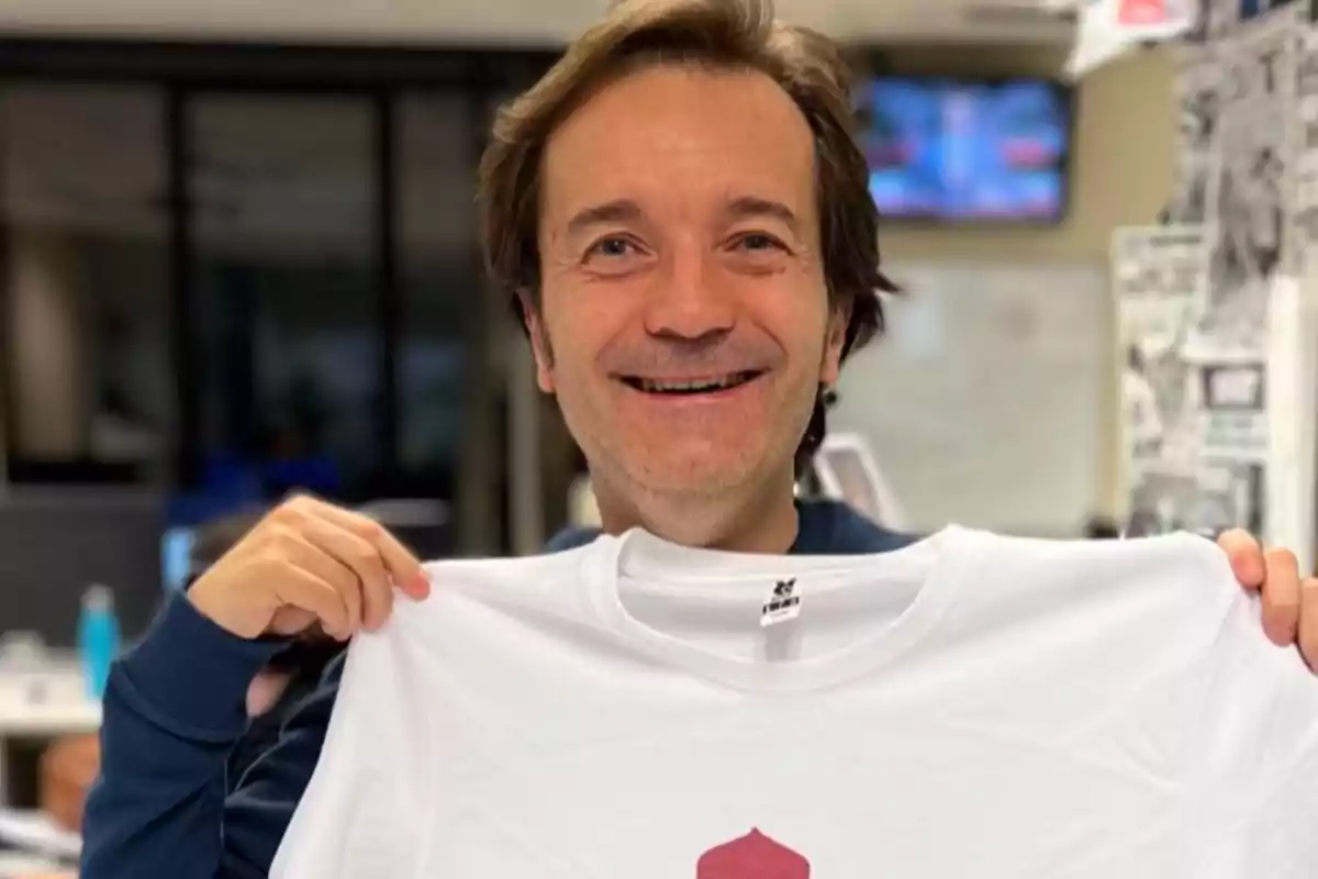 Un hombre sonriente sostiene una camiseta blanca en una oficina.