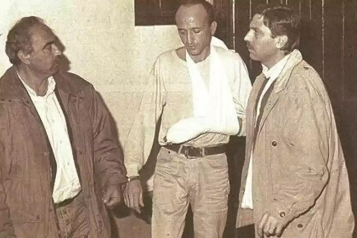Tres hombres de pie, uno de ellos con el brazo enyesado y vendado, en una imagen en blanco y negro. Tres hombres de pie, uno de ellos con el brazo enyesado y vendado, en una imagen en blanco y negro.