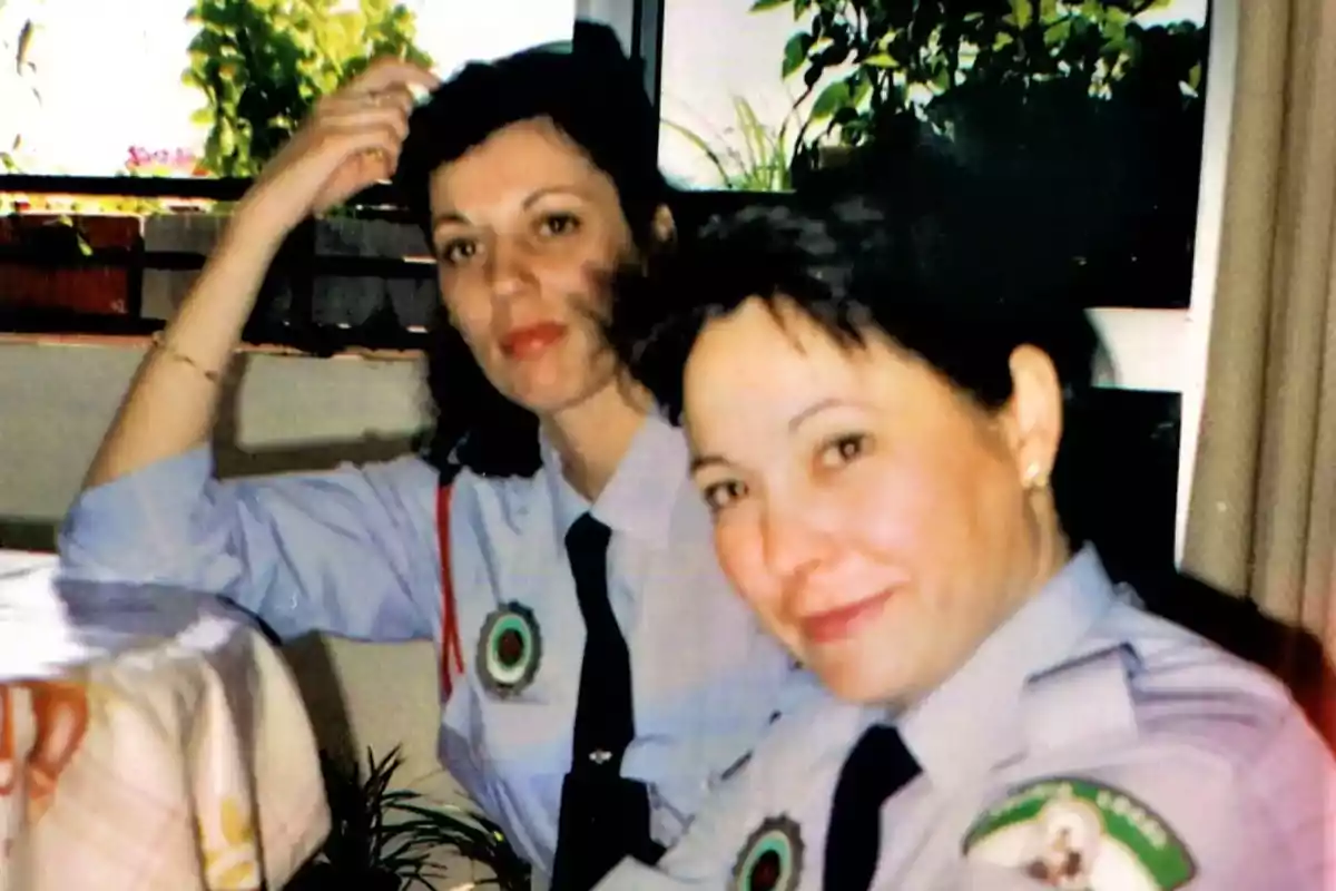 Dos mujeres con uniformes de policía sentadas en una mesa con plantas al fondo. Dos mujeres con uniformes de policía sentadas en una mesa con plantas al fondo.
