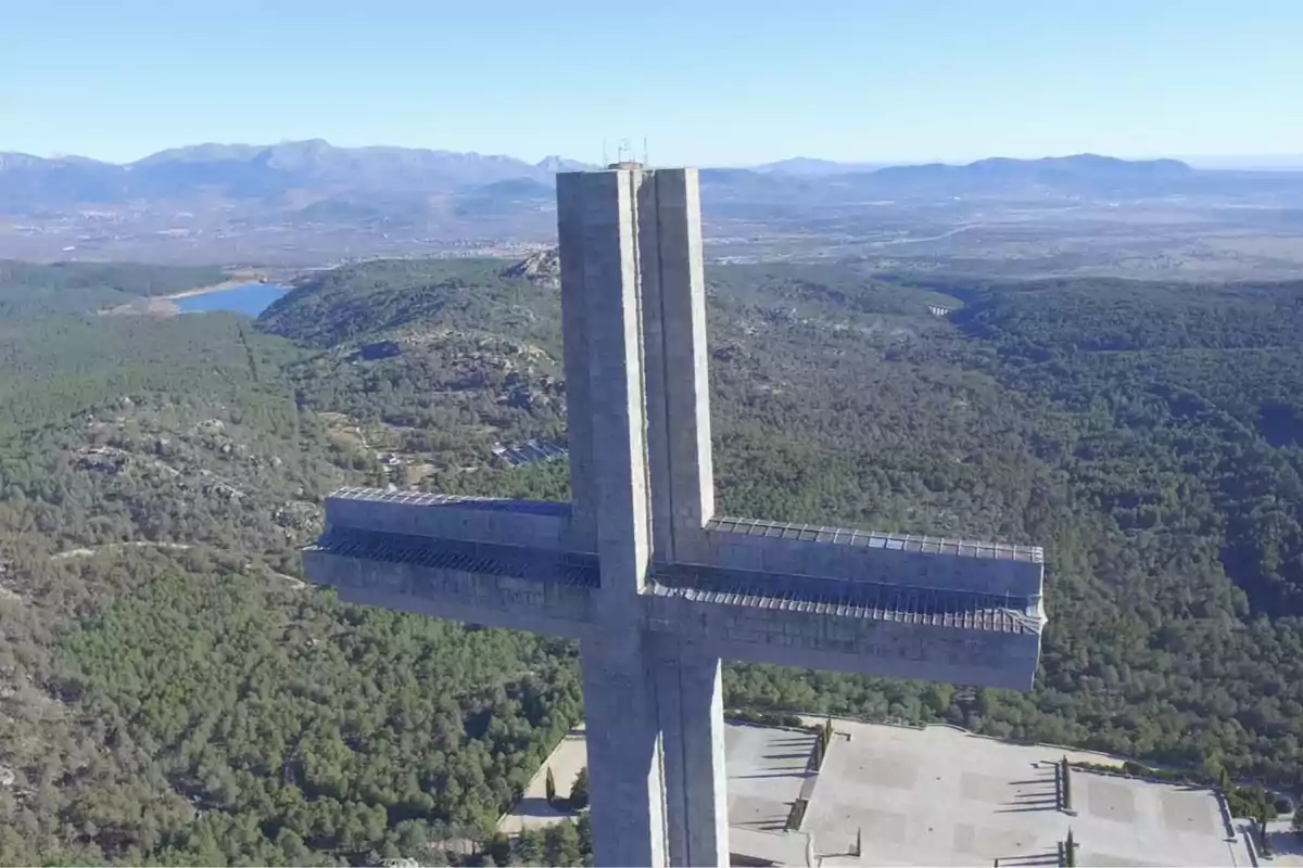 Vista aérea de una gran cruz de piedra en un paisaje montañoso con vegetación y un lago en el fondo. Vista aérea de una gran cruz de piedra en un paisaje montañoso con vegetación y un lago en el fondo.
