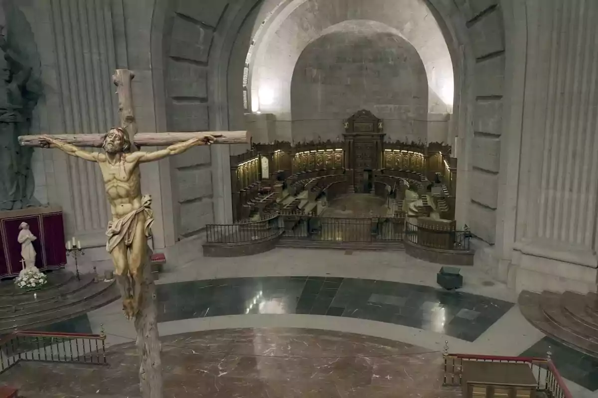 Una imagen de un crucifijo en el interior de una iglesia con un altar y un coro de madera al fondo. Una imagen de un crucifijo en el interior de una iglesia con un altar y un coro de madera al fondo.