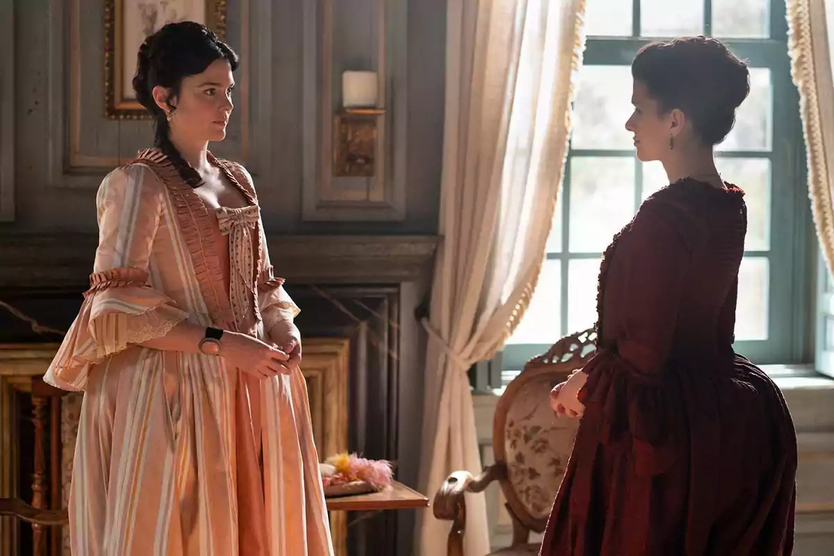 Dos mujeres vestidas con trajes de época se miran en una habitación elegante con cortinas y muebles antiguos. Captura de 'Valle Salvaje' Dos mujeres vestidas con trajes de época se miran en una habitación elegante con cortinas y muebles antiguos. Captura de 'Valle Salvaje'