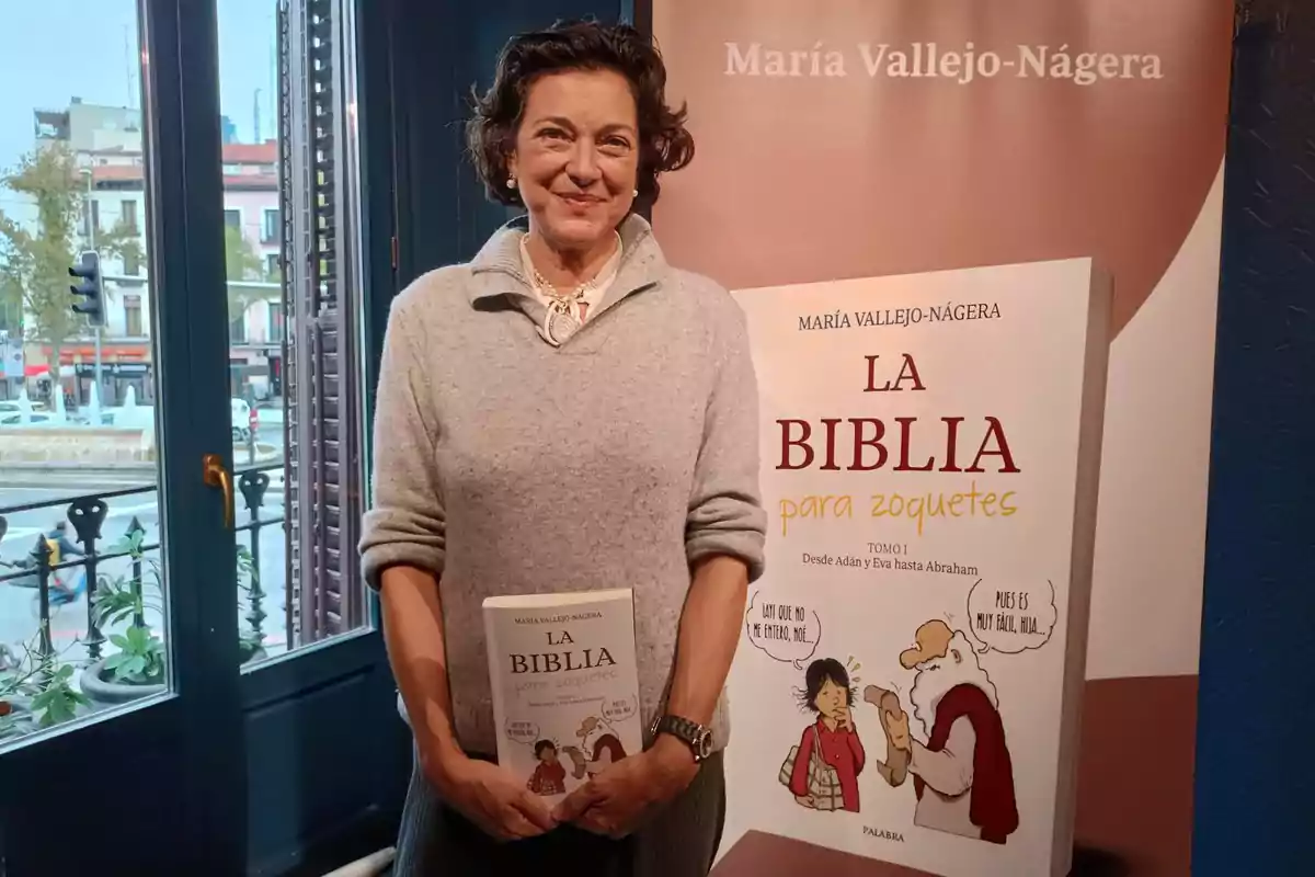 Una persona sosteniendo un libro titulado "La Biblia para zoquetes" de María Vallejo-Nágera, con un cartel del mismo libro en el fondo.