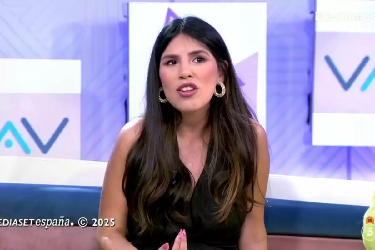 Isa Pantoja con cabello largo y oscuro está sentada en un set de televisión hablando, lleva un vestido negro y pendientes grandes, el fondo tiene un diseño geométrico y logotipos. Captura de 'Vamos a ver'