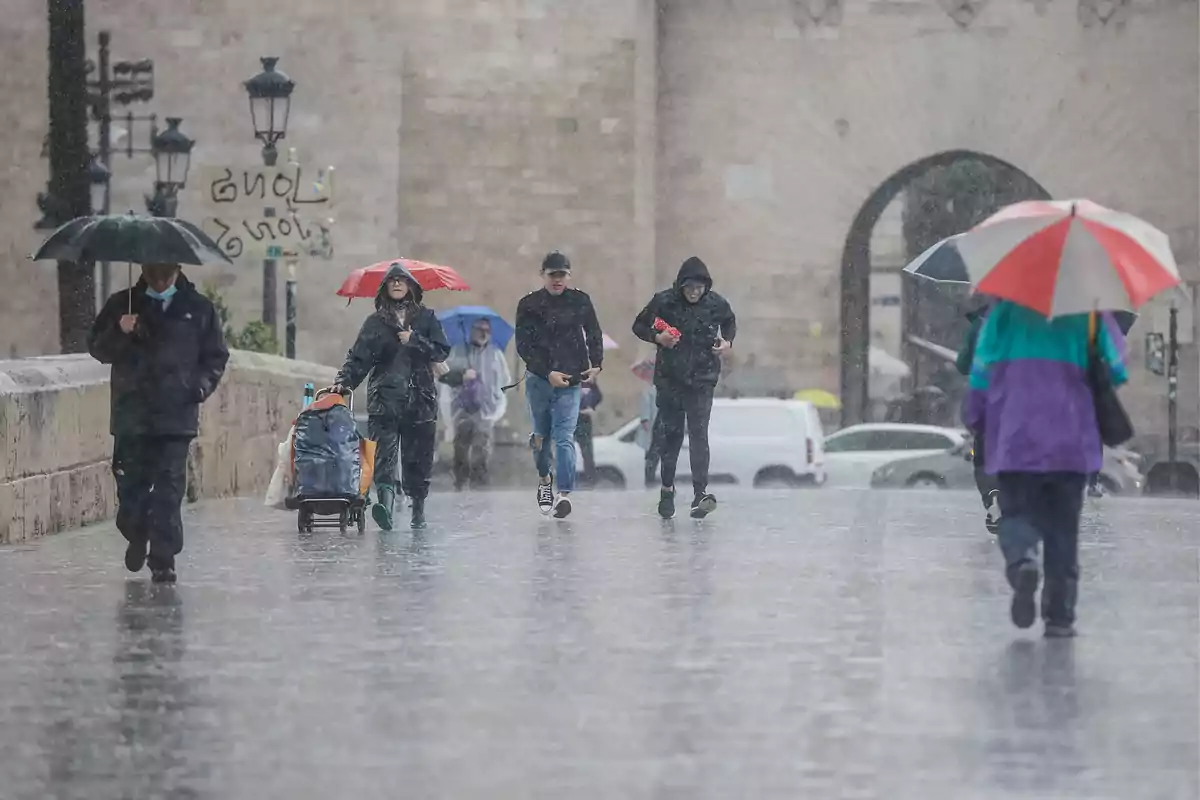 Personas caminando bajo la lluvia con paraguas en una calle urbana.