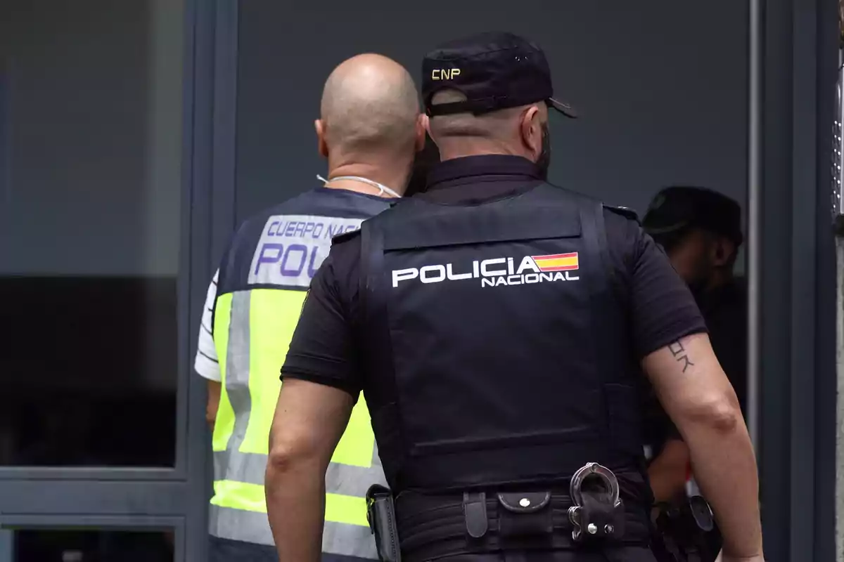 Dos agentes de la Policía Nacional de espaldas entrando a un edificio.