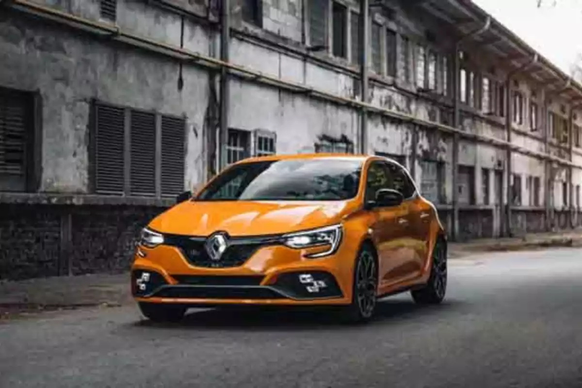 Un coche deportivo naranja estacionado frente a un edificio industrial antiguo.