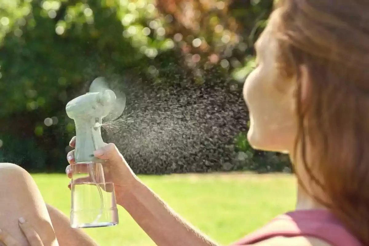 Persona usando un ventilador de mano con spray de agua en un día soleado al aire libre.