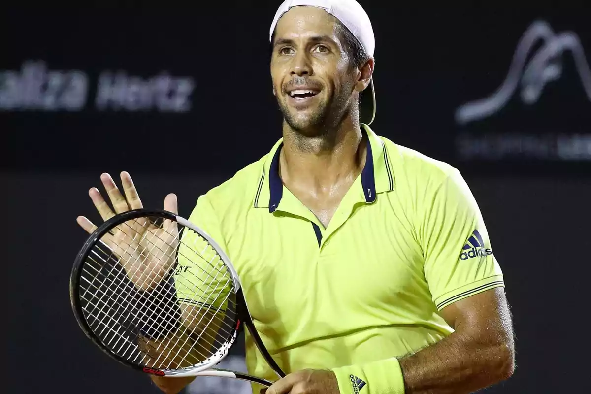 Tenista con camiseta amarilla y gorra blanca sosteniendo una raqueta en una cancha de tenis.