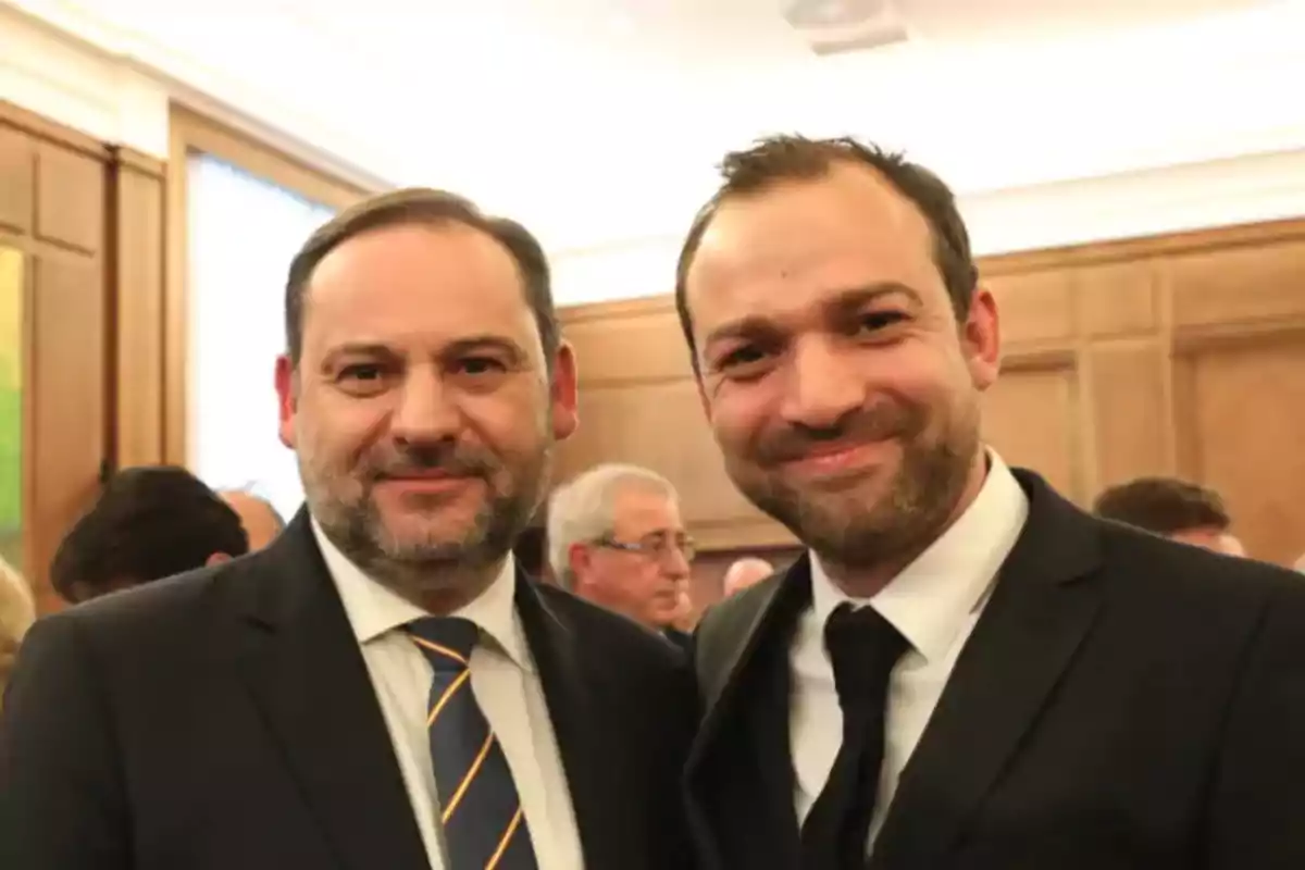 Dos hombres vestidos de traje sonríen en un evento social.