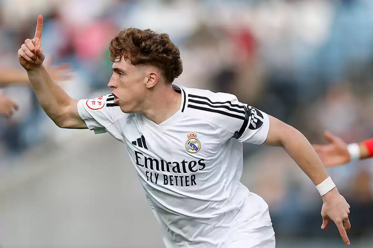 Un jugador de fútbol con uniforme blanco celebra levantando un dedo mientras corre en el campo. Un jugador de fútbol con uniforme blanco celebra levantando un dedo mientras corre en el campo.
