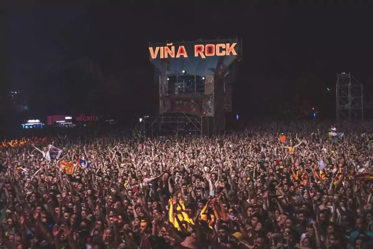 Una multitud de personas disfrutando de un concierto al aire libre durante la noche con un gran escenario iluminado al fondo.
