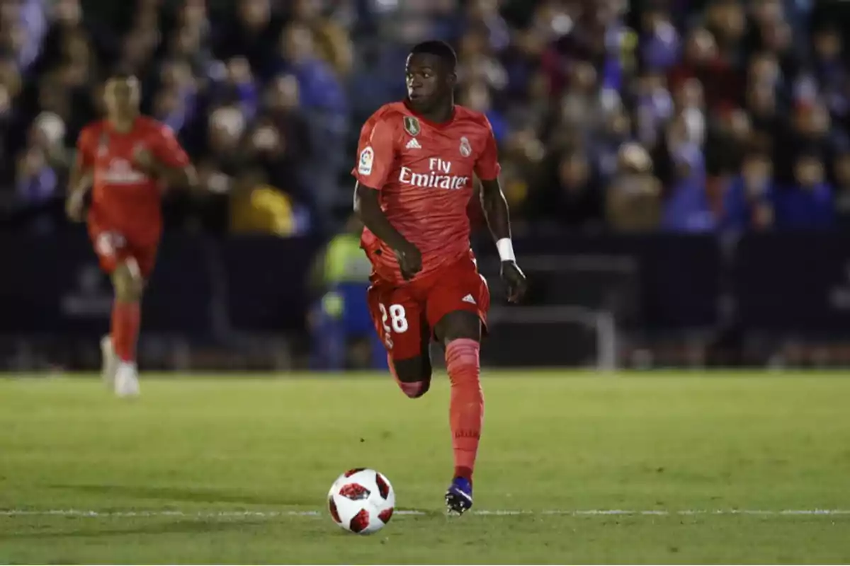 Un jugador de fútbol con uniforme rojo corre con el balón en un campo durante un partido. Un jugador de fútbol con uniforme rojo corre con el balón en un campo durante un partido.