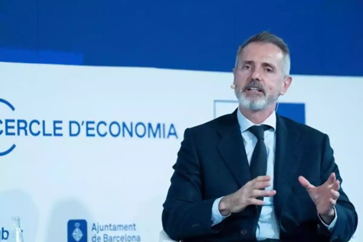 Gray-haired, bearded man speaking at an economic event with a blue and white background that reads Cercle d’Economia