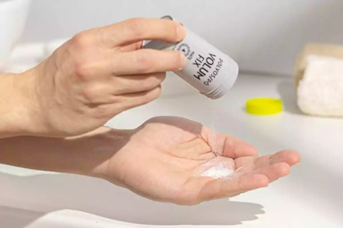 Persona vertiendo polvo blanco en la palma de su mano desde un envase cilíndrico en un baño. Persona vertiendo polvo blanco en la palma de su mano desde un envase cilíndrico en un baño.