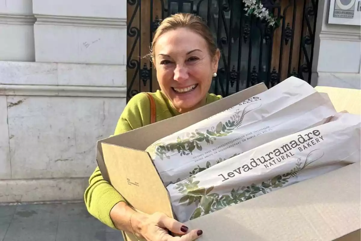 Una mujer sonriente sostiene una caja con baguettes de una panadería llamada Levaduramadre.