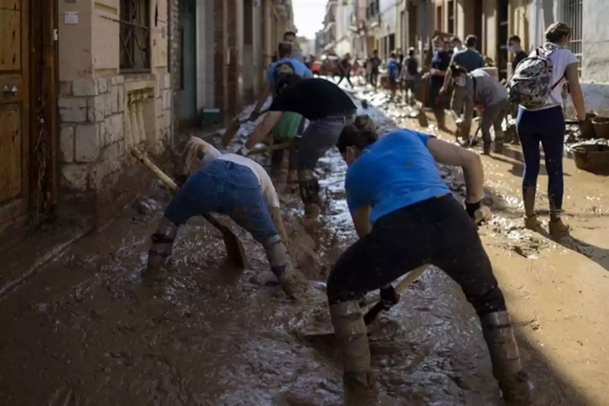 Personas limpiando una calle llena de barro después de una inundación.