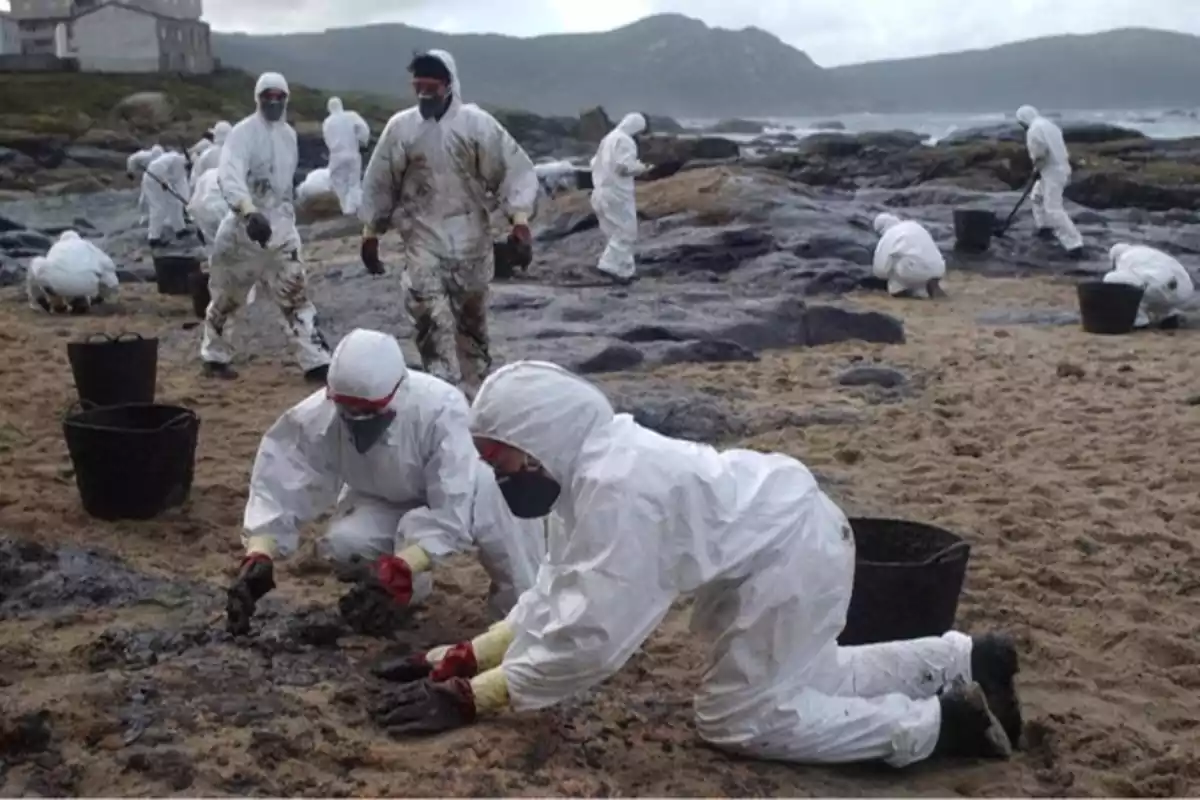 Personas con trajes protectores limpian una playa afectada por un derrame de petróleo.