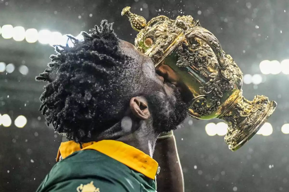 Un jugador de rugby besa un trofeo dorado ornamentado bajo las luces del estadio.